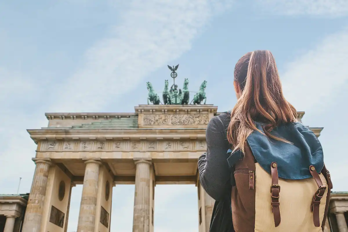 A tourist girl with a backpack or student looking at the Brandenburg Gate in Berlin in Germany.